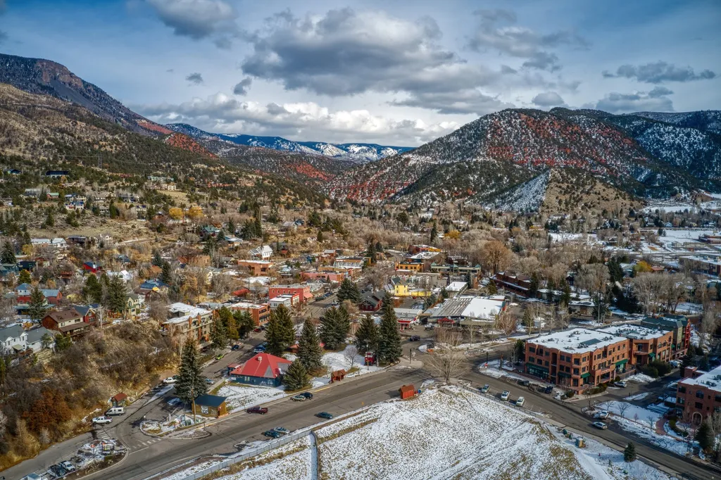 Aerial view of a small mountain town surrounded by colorful autumn foliage and snow-capped mountains.