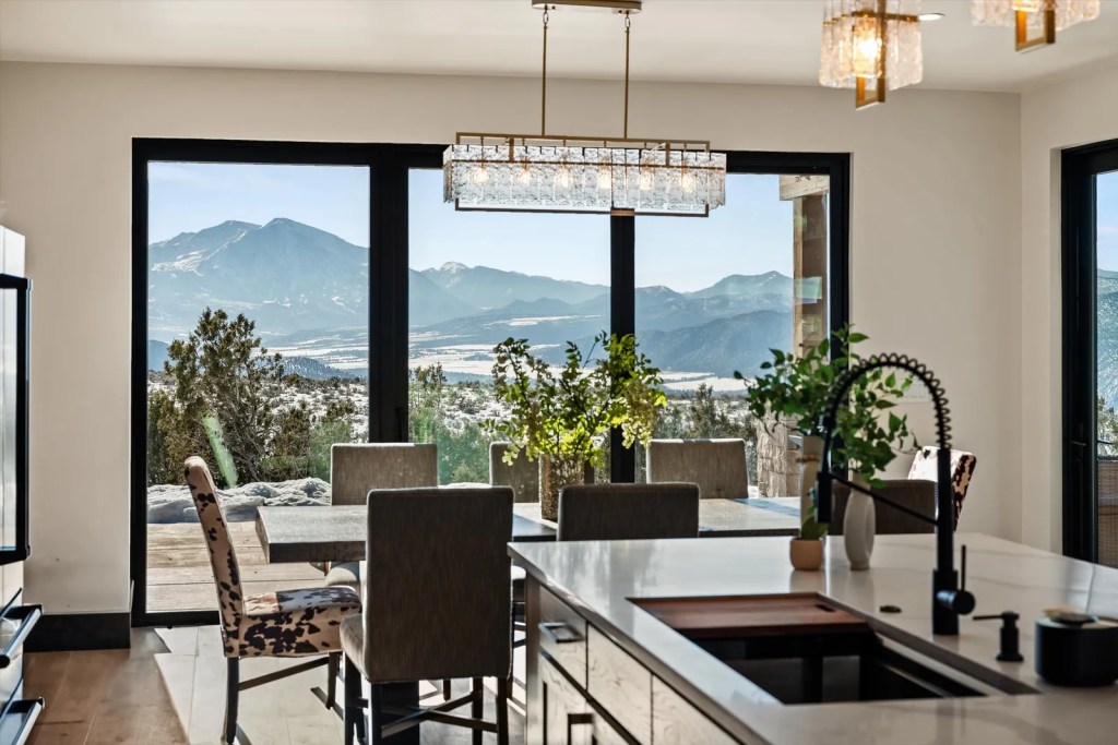Modern kitchen with a mountain view, featuring a dining table, potted plants, and large windows allowing natural light.